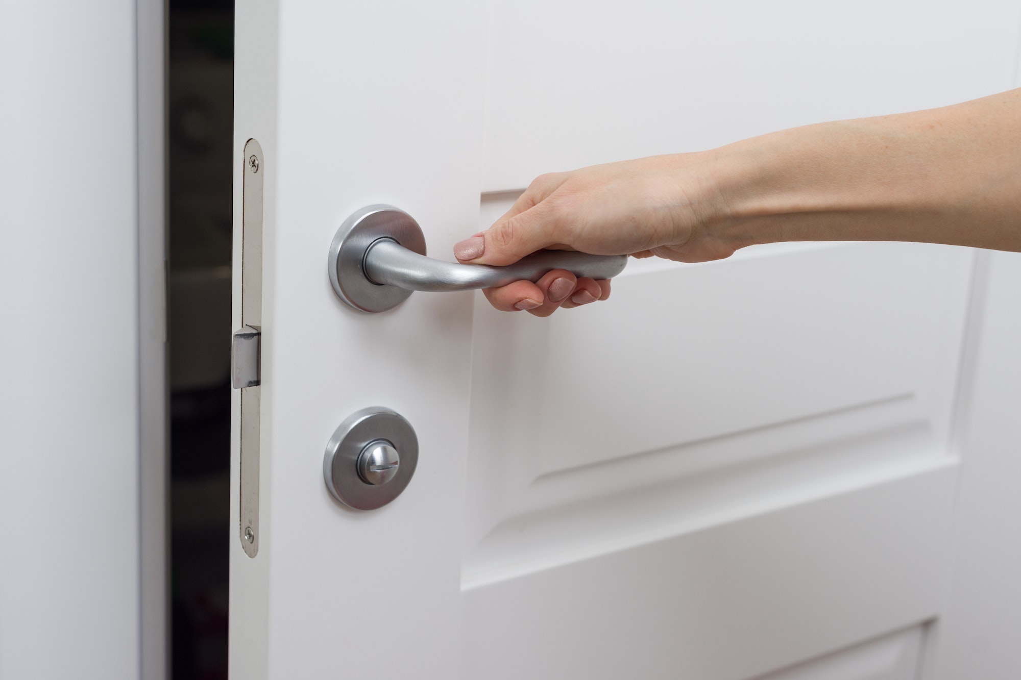 The hand opens the door slightly. Detail of a white interior door with a chrome door handle and